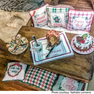 May include: A miniature Christmas scene with a wooden table, pillows with festive embroidery, and a variety of treats, including a panettone, cookies, and a cake. The pillows feature the phrases "Bonne Ann&eacute;e", "No&euml;l", and "Joyeux No&euml;l".
