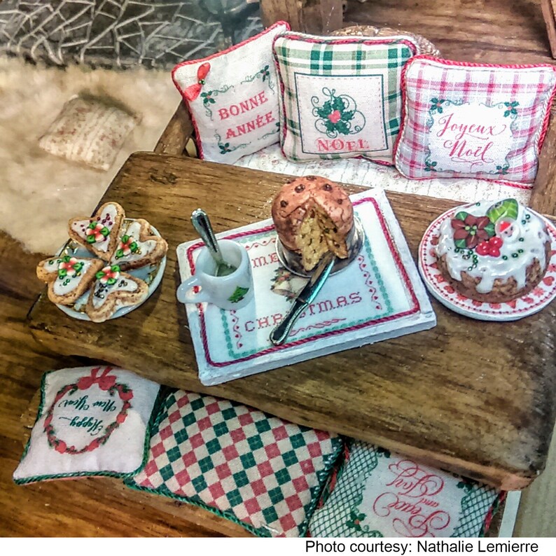 May include: A miniature Christmas scene with a wooden table, pillows with festive embroidery, and a variety of treats, including a panettone, cookies, and a cake. The pillows feature the phrases "Bonne Ann&eacute;e", "No&euml;l", and "Joyeux No&euml;l".