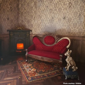 May include: A red velvet tufted sofa with wooden legs sits in a room with a fireplace and a patterned rug. A skeletal dog figurine sits on a small blue stool.