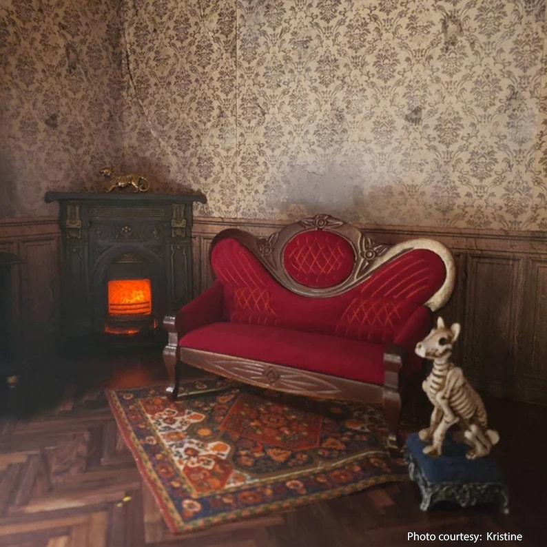 May include: A red velvet tufted sofa with wooden legs sits in a room with a fireplace and a patterned rug. A skeletal dog figurine sits on a small blue stool.