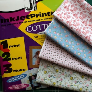 May include: Four different patterned cotton fabrics for inkjet printing. The fabrics are stacked on top of each other, with the top fabric being a red and white floral pattern. The second fabric is a light blue floral pattern. The third fabric is a pink floral pattern with white dots. The fourth fabric is a green and white floral pattern with butterflies. The fabrics are labeled "InkJet Printing" and "Cotton".