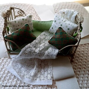 May include: A white metal doll bed with a green and white striped mattress and pillows. The pillows are covered in green plaid fabric, white lace, and a white fabric with green shamrocks.