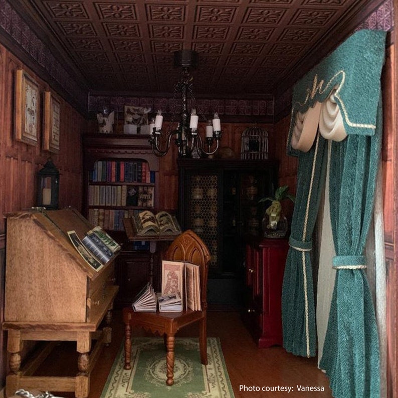 May include: A miniature dollhouse room with a dark wood desk, bookshelves, and a chandelier. The room is decorated with a green rug, a green curtain with a white trim, and a birdcage. The text "Photo courtesy: Vanessa" is visible in the bottom right corner of the image.