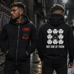 Puede incluir: Sudadera con capucha negra con cremallera, con un lobo rojo y negro y el texto "LONE WOLF" en la parte delantera. La parte trasera presenta un lobo entre ovejas con el texto "NOT ONE OF THEM". La sudadera tiene capucha y bolsillos delanteros.