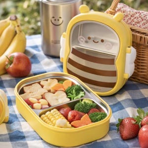 Pu&ograve; includere: Un portapranzo giallo a forma di ape, pieno di pane, broccoli e mais. &Egrave; visibile anche un thermos in acciaio inossidabile con una faccina sorridente, insieme alla frutta.
