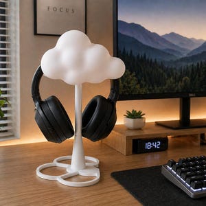 Könnte beinhalten: Ein weißer, wolkenförmiger Kopfhörerständer hält ein Paar schwarze Over-Ear-Kopfhörer. Der Ständer steht auf einem Holzschreibtisch, im Hintergrund ein Computermonitor und eine Tastatur. Das Wort "FOCUS" ist auf einem gerahmten Bild zu sehen.