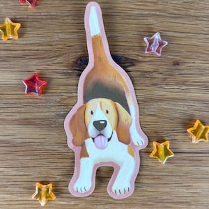 Könnte beinhalten: Ein gestanzter Aufkleber, der einen braun-weiß-schwarzen Beagle in einer spielerischen Verbeugungsposition mit nach oben gerichtetem Schwanz zeigt. Der Hund hat Schlappohren, eine weiße Schnauze und eine sichtbare rosa Zunge. Mehrere kleine sternförmige Perlen.