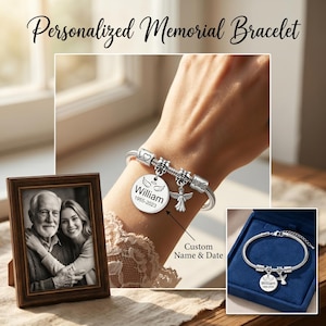K&ouml;nnte beinhalten: Ein silbernes Charm-Armband mit einem runden Anh&auml;nger, der mit einem Namen und Daten graviert ist, und einem Engels-Charm. Das Armband wird mit einem gerahmten Schwarz-Wei&szlig;-Foto und einem Armband in einer blauen Box pr&auml;sentiert. Der Text lautet "Personalized Memorial Bracelet."