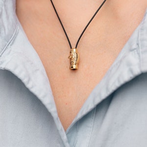 May include: A gold necklace with a detailed pendant shaped like a totem pole. The pendant is hanging from a black cord.