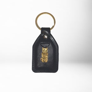 May include: Black leather keychain with a gold-colored cat charm. The keychain has a metal ring for attaching keys.
