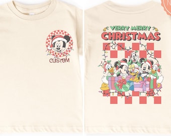 May include: A natural-colored t-shirt featuring a front graphic of Mickey Mouse in a Santa hat inside a red and white checkered circle with the word CUSTOM, and a back graphic of Disney characters with gifts, lights, and the text VERRY MERRY CHRISTMAS.