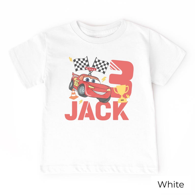 May include: A white short-sleeve t-shirt featuring a graphic of a red race car, two checkered flags, a gold trophy, and an orange traffic cone. The design includes the large red number 3 and the name JACK in bold red capital letters.