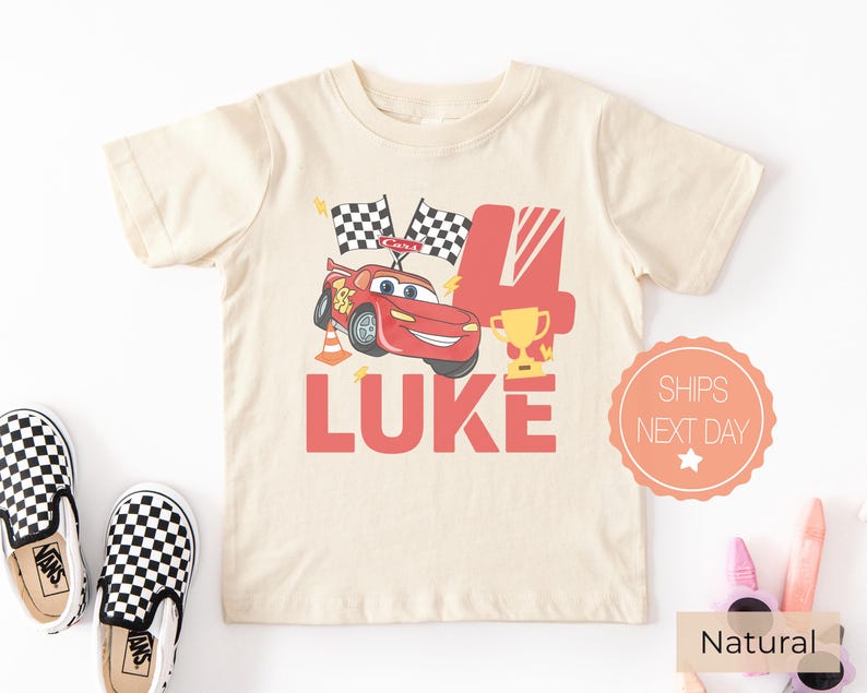 May include: A cream-colored short-sleeve t-shirt featuring a graphic of a red race car, two checkered flags, a gold trophy, and an orange traffic cone. The design includes the large red number 4 and the name LUKE in bold red capital letters.