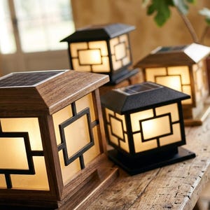 Op de afbeelding: Verschillende op zonne-energie werkende buitenlantaarns met een houten frame en zwarte accenten worden getoond op een houten oppervlak. De lantaarns hebben een geometrisch ontwerp en een warme, uitnodigende gloed. Elke lantaarn heeft een zonnepaneel.