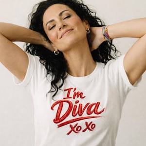 May include: White t-shirt with the text "I'm Diva" in red script. The shirt also features "Xo Xo" in red. The person in the image has dark curly hair and is wearing gold hoop earrings and a colourful bracelet.