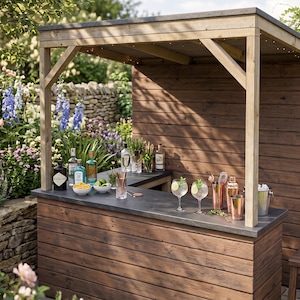 Può includere: Bar in legno all'aperto con un piano di lavoro grigio scuro, fornito di bottiglie, bicchieri e strumenti per cocktail. Il bar è circondato da una vegetazione lussureggiante e fiori, creando un'atmosfera rilassante. Due sgabelli in legno sono posti davanti al bar.