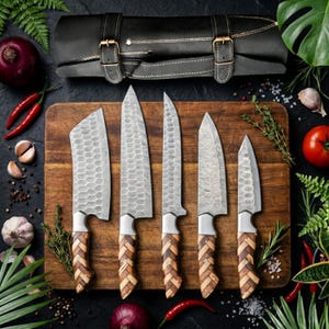 Könnte beinhalten: Ein Set aus fünf Edelstahl-Küchenmessern mit Holzgriffen, angeordnet auf einem Holzschneidebrett. Die Klingen haben ein strukturiertes Muster. Eine schwarze Leder-Messertasche ist im Hintergrund zu sehen, zusammen mit frischem Gemüse und Kräutern.
