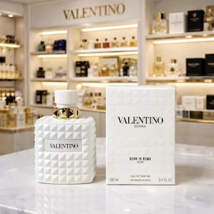 May include: A white Valentino perfume bottle and box. The bottle has a geometric design and gold accents. The box reads "VALENTINO DONNA BORN IN ROMA NORY" and indicates 3.4 fl oz. The perfume is displayed in a well-lit store setting.