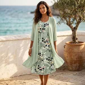 Peut inclure: Une robe vert clair à motifs floraux, associée à un cardigan transparent assorti. La robe présente un ourlet au genou et un col rond. Le cardigan a des manches trois-quarts. La tenue est portée en extérieur, près de la mer.