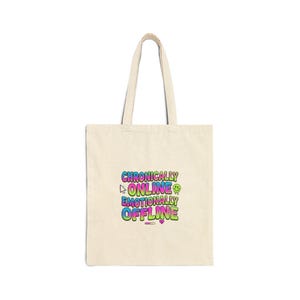 May include: A cream-coloured tote bag featuring the text "Chronically Online Emotionally Offline" in a vibrant, gradient font. The bag has two handles and is made of a durable fabric. The design incorporates a cursor, smiley face, and a heart symbol.