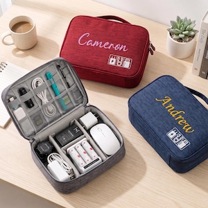 May include: Three rectangular zippered travel organizers in red, blue, and gray. The red case features the name Cameron, the blue case features the name Andrew, and the gray case is open, revealing internal elastic loops and compartments holding various electronic accessories, cables, batteries, and a white computer mouse.