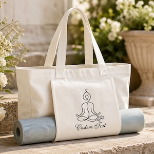 Op de afbeelding: Een crèmekleurige canvas draagtas met twee stevige handvatten en een voorvak ontworpen om een opgerolde lichtblauwe yogamat vast te houden. Het voorvak toont een zwarte lijntekening van een persoon in lotushouding met de tekst Custom Text.