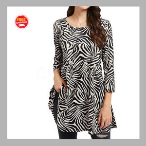 May include: A long-sleeved tunic top featuring a black and white zebra stripe pattern. The garment has a round neckline and a relaxed, flowing fit that extends past the waist, with visible side pockets integrated into the hemline.