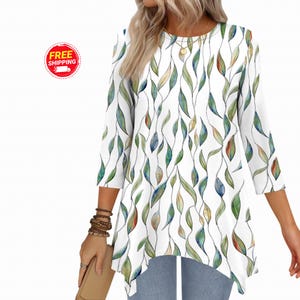 May include: White tunic top with a three-quarter sleeve and a leaf pattern in shades of green, blue, and orange. The top has a rounded neckline and an asymmetrical hemline.