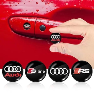 May include: Black and red Audi car door lock pin covers. The covers feature the Audi logo in white, and the S line and RS logos in red and white. The car door is red.