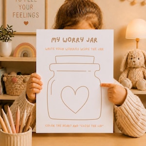 May include: A child holds a white paper with the words "MY WORRY JAR" and instructions to write worries inside a jar, color a heart, and close the lid. The image includes colored pencils, a framed print, and a stuffed animal.
