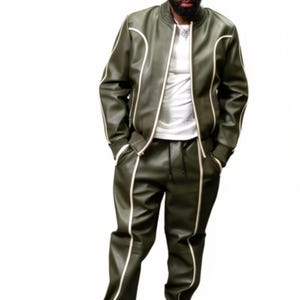May include: Olive green leather bomber jacket and matching pants with white trim. The jacket has a zipper closure and the pants have a drawstring waist. The outfit is paired with white sneakers.