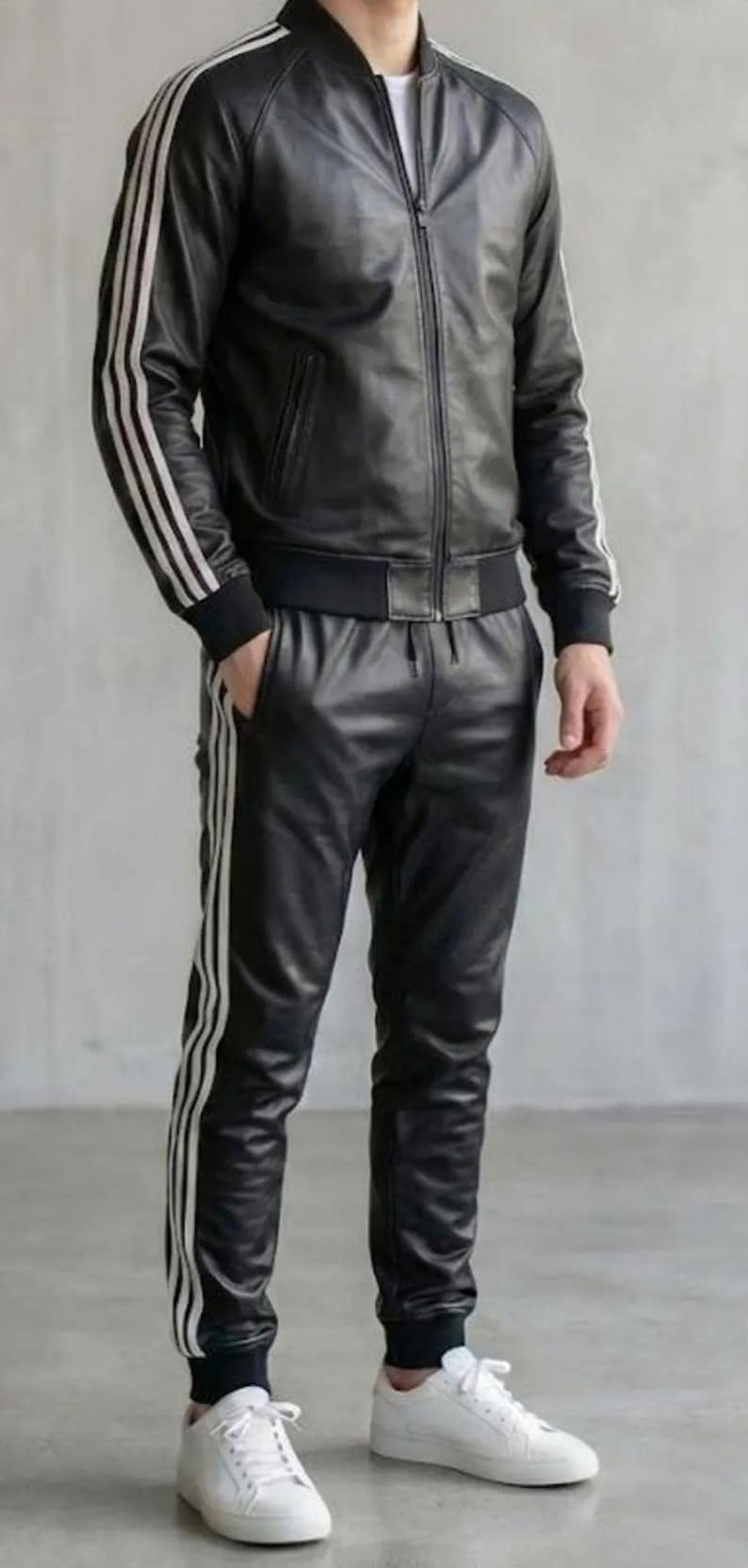 May include: Black leather tracksuit featuring white stripes on the jacket sleeves and trouser legs. The jacket is a bomber style with a zip closure. The trousers have a drawstring waist and the person is wearing white trainers.