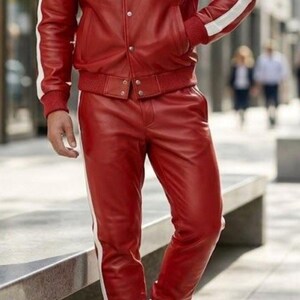 May include: A red leather jacket and trousers set with white stripes. The jacket features a button closure and pockets. The trousers have an elasticated waist and cuffs. The outfit is completed with white trainers.