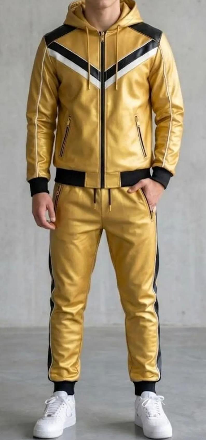 May include: A gold tracksuit featuring a hooded jacket and matching trousers. The jacket has black and white shoulder detailing and a zip. The trousers have a black stripe down the side. The outfit is made of a shiny material, suitable for casual wear.