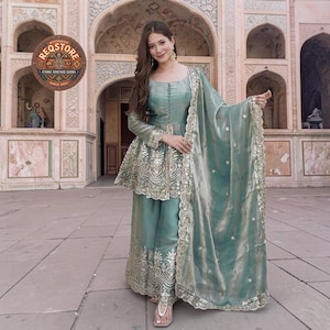 Peut inclure: Un ensemble salwar kameez brodé de couleur sarcelle. La tenue comprend un haut tunique avec un basque, un pantalon large et une dupatta assortie. La tenue est ornée de broderies dorées et est portée avec des sandales.