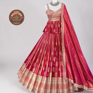 May include: A vibrant fuchsia lehenga set featuring a sleeveless peplum-style bodice and a voluminous pleated skirt, both adorned with intricate gold metallic embroidery. A matching fuchsia dupatta with a gold border is draped over the shoulder.