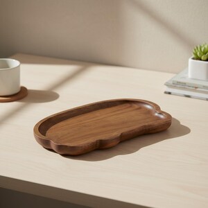 Peut inclure: Un plateau de service en bois en forme de nuage. Le plateau est en bois brun foncé et a une finition lisse et polie. Le plateau est posé sur une surface en bois de couleur claire.