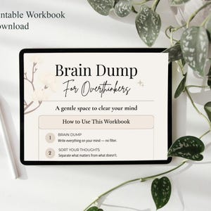 May include: A digital tablet shows a printable workbook titled "Brain Dump For Overthinkers." The workbook's instructions are visible, along with a stylus. The image is set against a white background, with leafy green plants in the upper right corner.