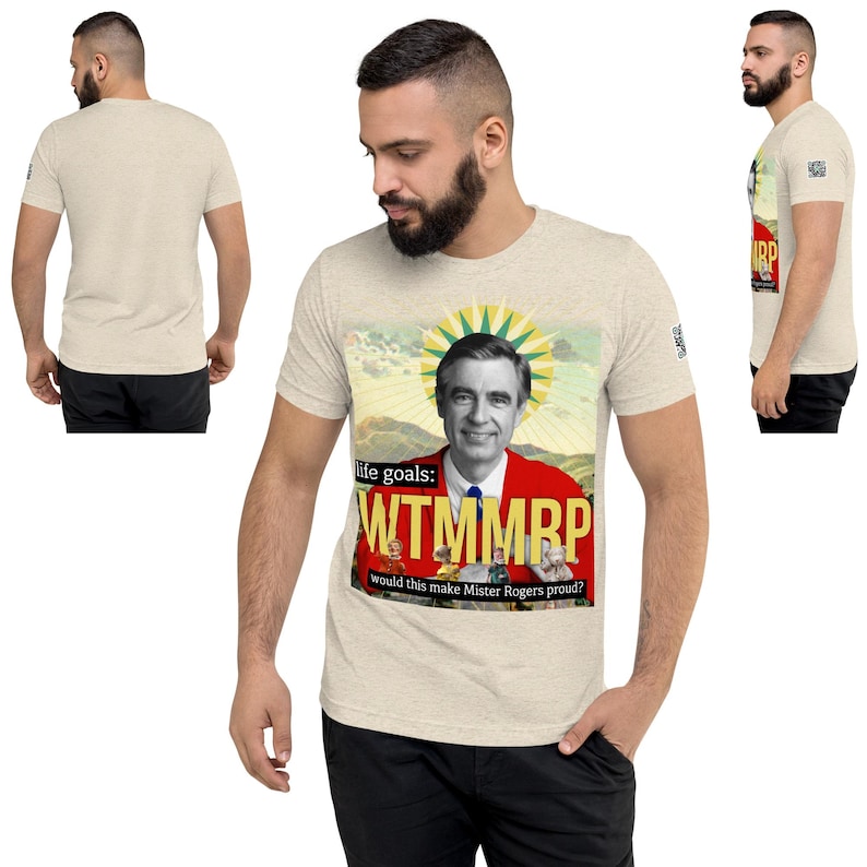 May include: Beige short-sleeve t-shirt featuring a graphic of Fred Rogers in a red jacket with the text "life goals: WTMMRP would this make Mister Rogers proud?" The shirt is made of a soft, comfortable material.
