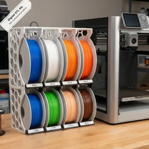 May include: A white 3D printed storage rack with a honeycomb side pattern holding eight spools of PLA filament in blue, white, orange, green, tan, and brown. A digital STL file not a physical product label is visible in the top left corner.