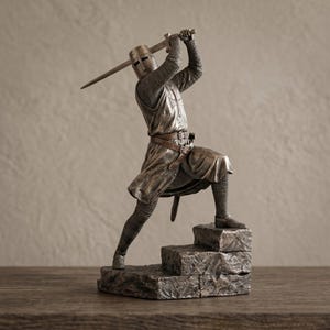 Puede incluir: Estatua plateada de un caballero con armadura completa, levantando una espada por encima de la cabeza. El caballero posa sobre un conjunto de escalones de piedra, con un casco y cota de malla detallados. Un cinturón de cuero marrón rodea la cintura.
