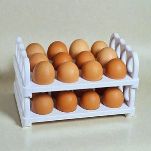 May include: A white plastic egg holder filled with brown eggs. The two-tiered rack has a decorative design on the sides and holds a total of 18 eggs. The eggs vary in color from light tan to dark brown.