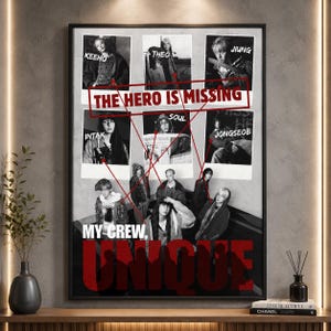 May include: A framed black and white poster featuring nine individuals, with text overlaying the image. The text includes "THE HERO IS MISSING" and "MY CREW, UNIQUE." The poster is displayed on a wooden shelf with decorative items.