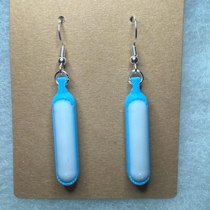 May include: A pair of earrings featuring a blue and white design. The earrings have a cylindrical shape with a blue top and bottom, and a white center. They hang from silver-colored ear wires.