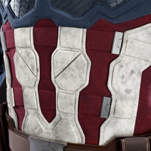 May include: Close-up of a Captain America costume chest piece. The design features a red and white colour scheme with a textured, weathered appearance. The chest piece is part of a larger costume.