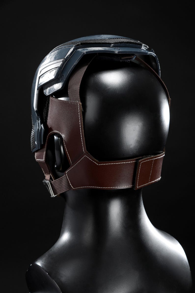 May include: A dark blue and silver helmet with a brown leather and fabric harness. The helmet is displayed on a black mannequin head. The harness has white stitching and a metal buckle.