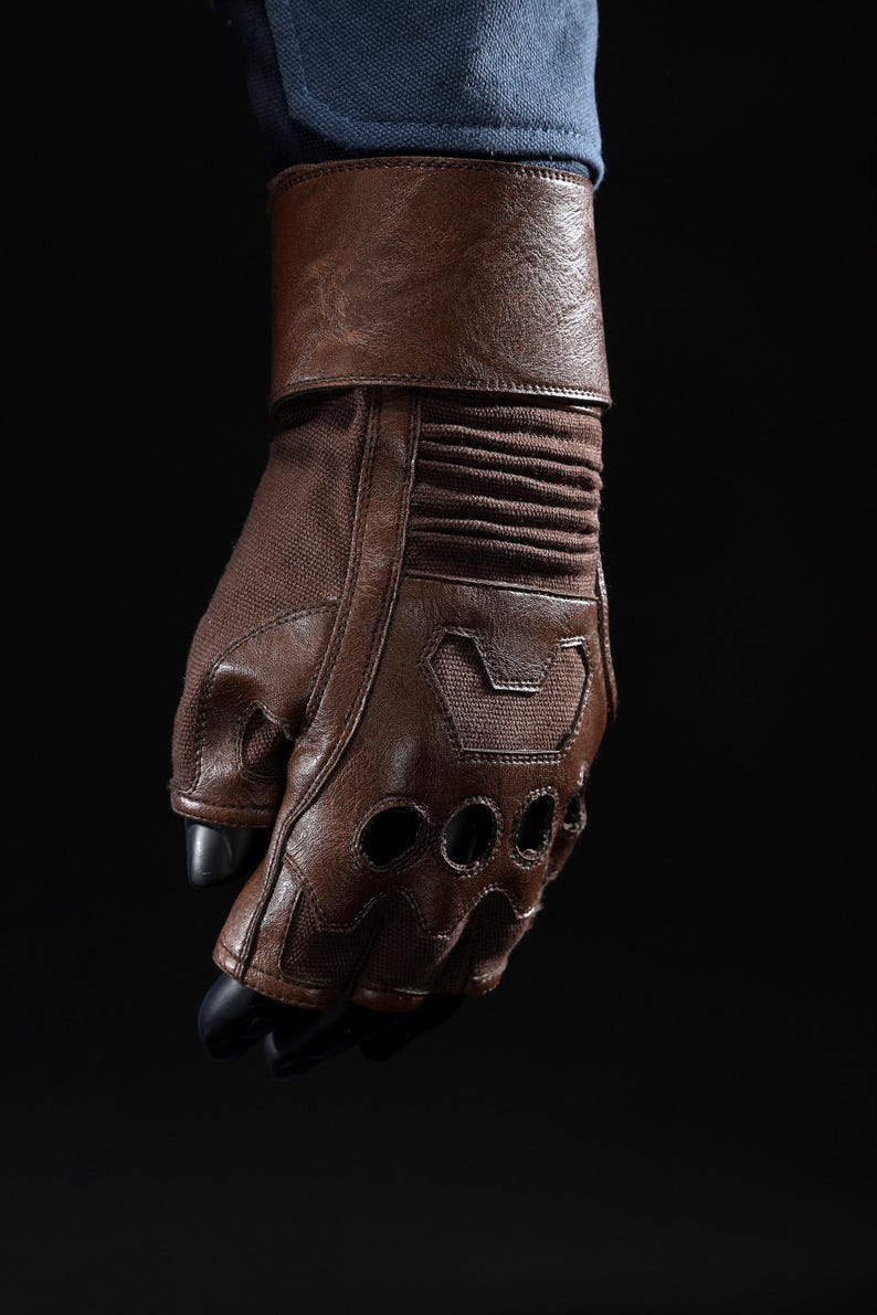 May include: Brown leather glove with fingerless design and ventilation holes. The glove features a padded wrist cuff and a textured fabric on the back of the hand. The fingers have black tips. The glove is worn over a blue sleeve.
