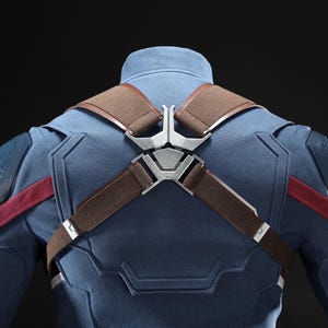 May include: A blue and red costume with brown straps and silver metal accents. The costume has a high collar and detailed shoulder and chest design. The back of the costume is visible against a dark background.
