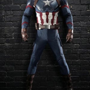 May include: A Captain America costume, with a blue and white star-spangled chest piece, red and white striped midsection, and blue trousers. The costume includes brown leather gloves, boots, and a belt. The outfit is displayed against a dark brick wall.