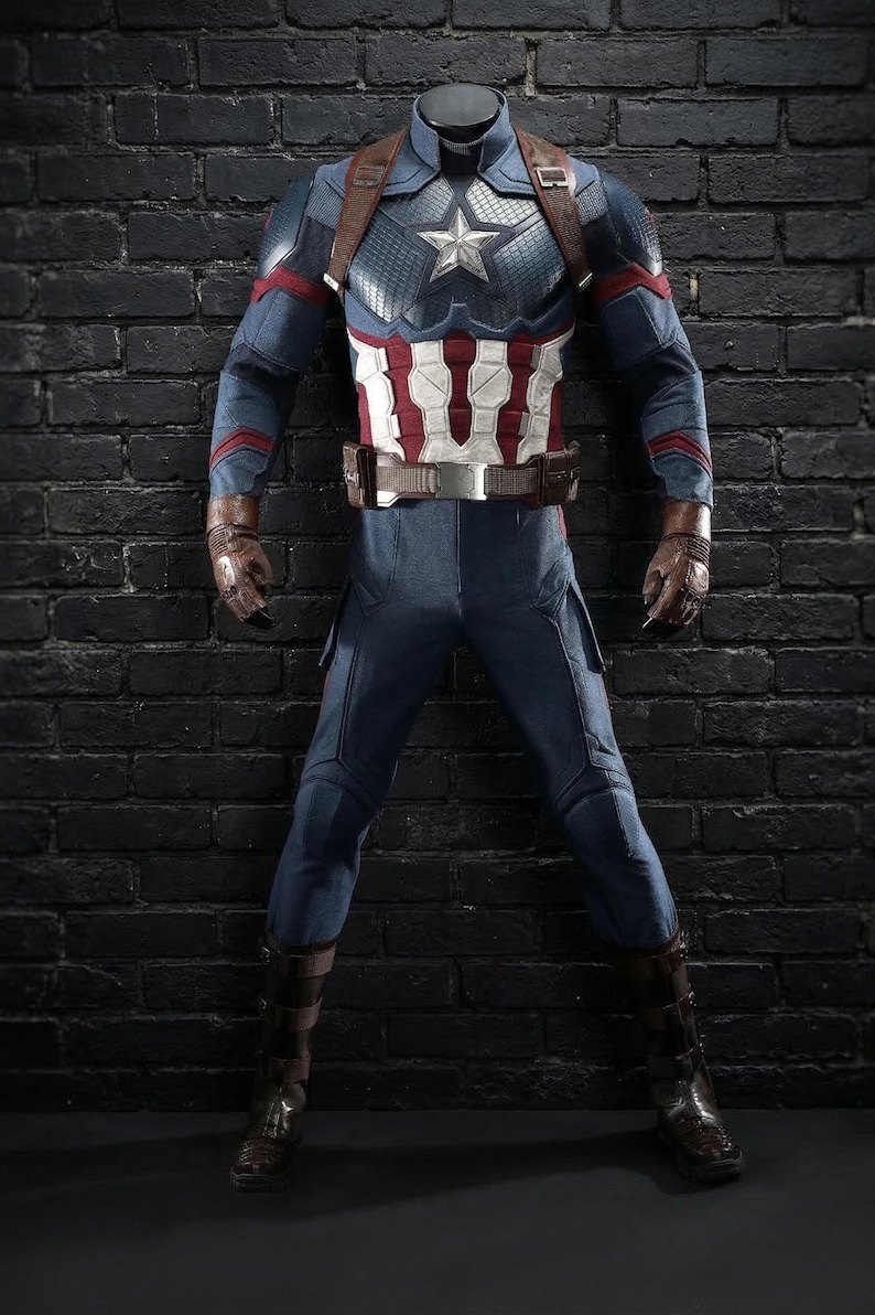 May include: A Captain America costume, with a blue and white star-spangled chest piece, red and white striped midsection, and blue trousers. The costume includes brown leather gloves, boots, and a belt. The outfit is displayed against a dark brick wall.